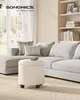A living room scene with a sectional sofa, decorative pillows, and a round ottoman. Produktbild-Vorschau