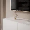 A white bust sculpture sits on top of a white cabinet, with a television screen visible in the background. Náhled obrázku produktu