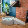 A children's ball pit and slide set in a living room with plants and a TV. Produktbild-Vorschau