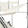 A cream-colored awning is shown extended from a black metal frame, with a crank mechanism visible on the right. Another awning is shown retracted in the background. Náhled obrázku produktu