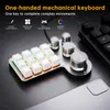 A close-up shot of a one-handed mechanical keyboard with RGB lighting and multiple control knobs, placed on a dark, textured surface next to a portion of a standard keyboard and a smartphone. Produktbild-Vorschau