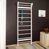 A white wooden climbing wall with teal straps and wooden rings attached, mounted on a dark ribbed wall in a room with a small cabinet and a framed picture. Voir les images du produit