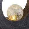 A close-up of a decorative solar light with a cracked glass sphere illuminated from within, resting on a dark, textured base. Anteprima dell’immagine prodotto