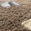 A close-up view of a fluffy brown rug with two gray slippers and a cream-colored fuzzy object. Produktbild-Vorschau