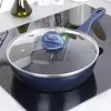 A dark blue frying pan with a glass lid and blue handle sits on a black induction stovetop. In the background, there are salt and pepper grinders and a bottle of olive oil on a shelf. Produktbild-Vorschau