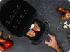 A hand is placing food into an open air fryer, surrounded by ingredients like carrots, tomatoes, garlic, and spices. Anteprima dell’immagine prodotto