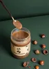 A jar of hazelnut spread with hazelnuts scattered around it. Produktbild-Vorschau