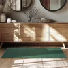 A green rug is placed on a wooden floor in front of a wooden dresser with decorative items on top. Produktbild-Vorschau