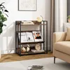 A three-tiered bookshelf with books, magazines, headphones, and a clock on it, placed in a living room setting next to a sofa. Produktbild-Vorschau