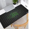 A gaming mousepad with a hexagonal pattern and green accents is shown on a desk next to a laptop and a plant. Náhled obrázku produktu
