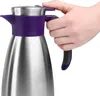 A hand is shown gripping the handle of a stainless steel thermal carafe with a purple accent. Produktbild-Vorschau