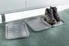 Three shoe trays are shown on a green carpet in front of a white cabinet. One tray has hiking boots on it. Produktbild-Vorschau