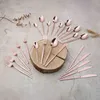 A set of rose gold cutlery is arranged on a textured surface, with some pieces resting on a wooden disc. Anteprima dell’immagine prodotto