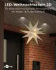 A large, illuminated star decoration hangs outside a brick building near a dark door. Produktbild-Vorschau