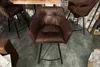 A bar stool in a rustic setting with a wooden table and brick wall. Produktbild-Vorschau