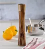 A wooden pepper mill is shown on a white surface with yellow bell peppers and a small pot in the background. Produktbild-Vorschau