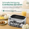 A countertop scene featuring an egg cooker, breakfast items, and a glass of orange juice. Produktbild-Vorschau