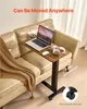 A mobile laptop table is placed next to a couch, with a laptop, headphones, and a cup on it. Produktbild-Vorschau
