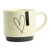 A cream-colored mug with a black heart design and a black base, set against a white background. Náhled obrázku produktu