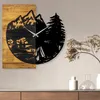 A wall clock with a mountain and camping scene is displayed on a wall above a wooden cabinet. Voir les images du produit