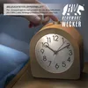 A hand is pressing the snooze button on a wooden alarm clock placed on a nightstand next to a bed. Produktbild-Vorschau