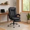 A black executive chair with a footrest is placed on a rug in front of a wooden desk and a window.