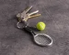A set of keys with a tennis racket and ball keychain on a dark gray textured surface. Náhled obrázku produktu