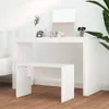 A white vanity table and stool set in a well-lit room, with a mirror and some makeup accessories on the table. A plant is visible to the right, and a bed is partially visible to the left. Produktbild-Vorschau
