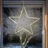 A star-shaped LED light decoration hangs in a window at night, with a blurred winter tree scene visible outside. Produktbild-Vorschau
