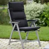 A black cushioned chair with a gray frame sits on a paved patio next to a grassy lawn with green bushes in the background. Produktbild-Vorschau