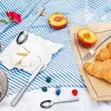 A picnic setting with cutlery, cheese, fruits, and croissants on a striped blanket. Produktbild-Vorschau