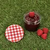 A jar of raspberry jam with raspberries and its lid on a grassy surface. Voir les images du produit