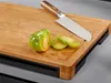 A green tomato is sliced on a bamboo cutting board next to a knife. Produktbild-Vorschau