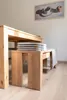 A wooden bench with cushions under a wooden table, with a painting on the wall in the background. Produktbild-Vorschau