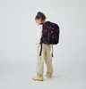 A young girl wearing a backpack and cargo pants, standing against a white background. Anteprima dell’immagine prodotto