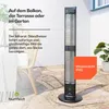 An outdoor patio scene with a tall, black infrared heater standing on a stone patio next to a wicker chair and a plant. Produktbild-Vorschau