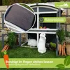 A two-story rabbit hutch with two rabbits inside, surrounded by grass, carrots, and lettuce. The image highlights the product's features and durability. Produktbild-Vorschau