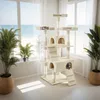 A multi-level cat tree is set up in a bright room with large windows overlooking the ocean. Plants are placed on either side of the cat tree. Voir les images du produit