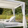 A white outdoor daybed with gray cushions and curtains is set up in a garden with lush greenery in the background. Produktbild-Vorschau
