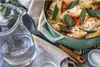 A close-up shot of a casserole dish filled with stuffed shells, garnished with sage leaves, next to a pitcher of water and a glass. Produktbild-Vorschau