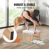 A woman is performing a yoga pose on a wooden yoga stool in a bright room. Voir les images du produit