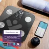 A digital scale and smartphone are displayed on a wooden floor, with a yoga mat in the background. Produktbild-Vorschau