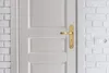 A close-up of a white door with a gold door handle, set against a white brick wall. Anteprima dell’immagine prodotto