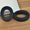 Two black headphone ear pads are placed on a wooden surface next to a laptop. Náhled obrázku produktu