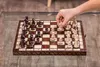 A hand is shown moving a white pawn on a wooden chessboard. Anteprima dell’immagine prodotto