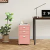 A pink filing cabinet with three drawers is placed next to a desk with a laptop and a lamp. Náhled obrázku produktu