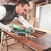A man is using a belt sander on a wooden table in a workshop. Podgląd zdjęcia produktu