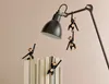 Four wooden monkey figurines are playfully interacting with a black desk lamp and a stack of books. Náhled obrázku produktu