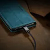 A close-up shot of a teal phone case with a charging cable plugged into the phone. Produktbild-Vorschau