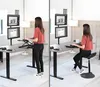 A woman is shown using a standing desk setup with dual monitors, first standing and then sitting on a stool. Náhľad obrázku produktu